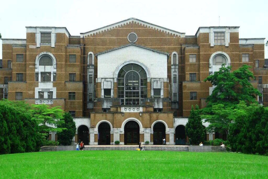 A classic university building surrounded by greenery, featuring a grand entrance and large windows.